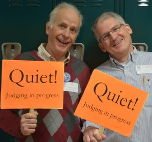 Two men holding signs that say Quiet, Judging in Progress.